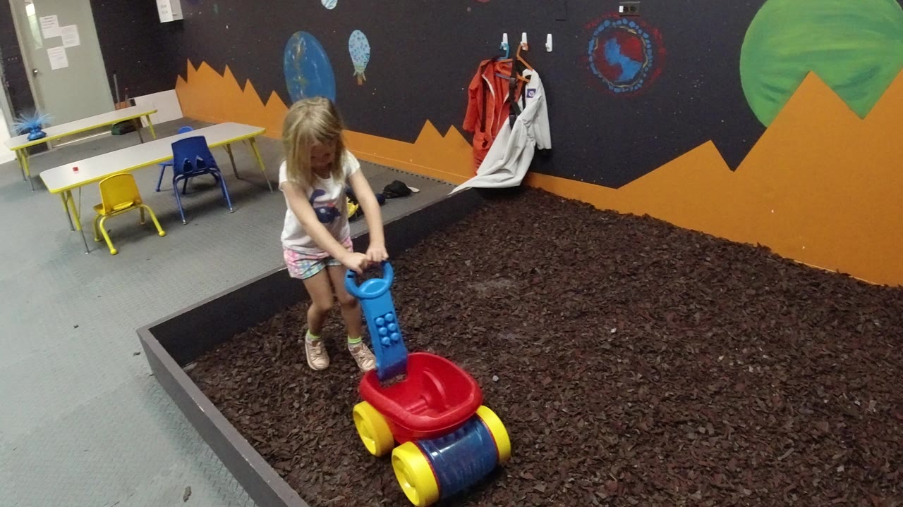 Young girl holding a colorful toy wagon in an indoor play area.