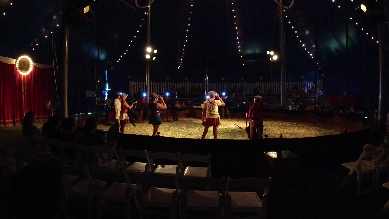 Young performers in a lit circus ring under string lights.