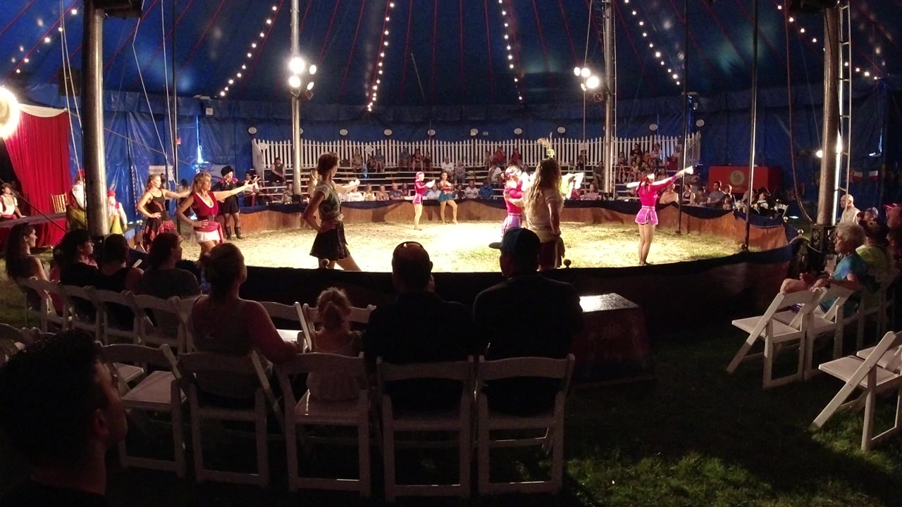 In Broomfield, Colorado, pink-dressed children spread across the ring while dark audience silhouettes and white folding chairs frame the foreground.