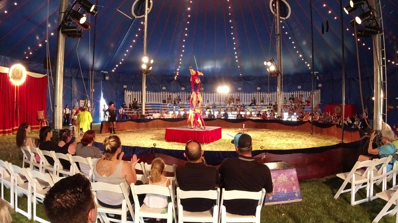 Circus acrobats balancing on a red platform before seated spectators.