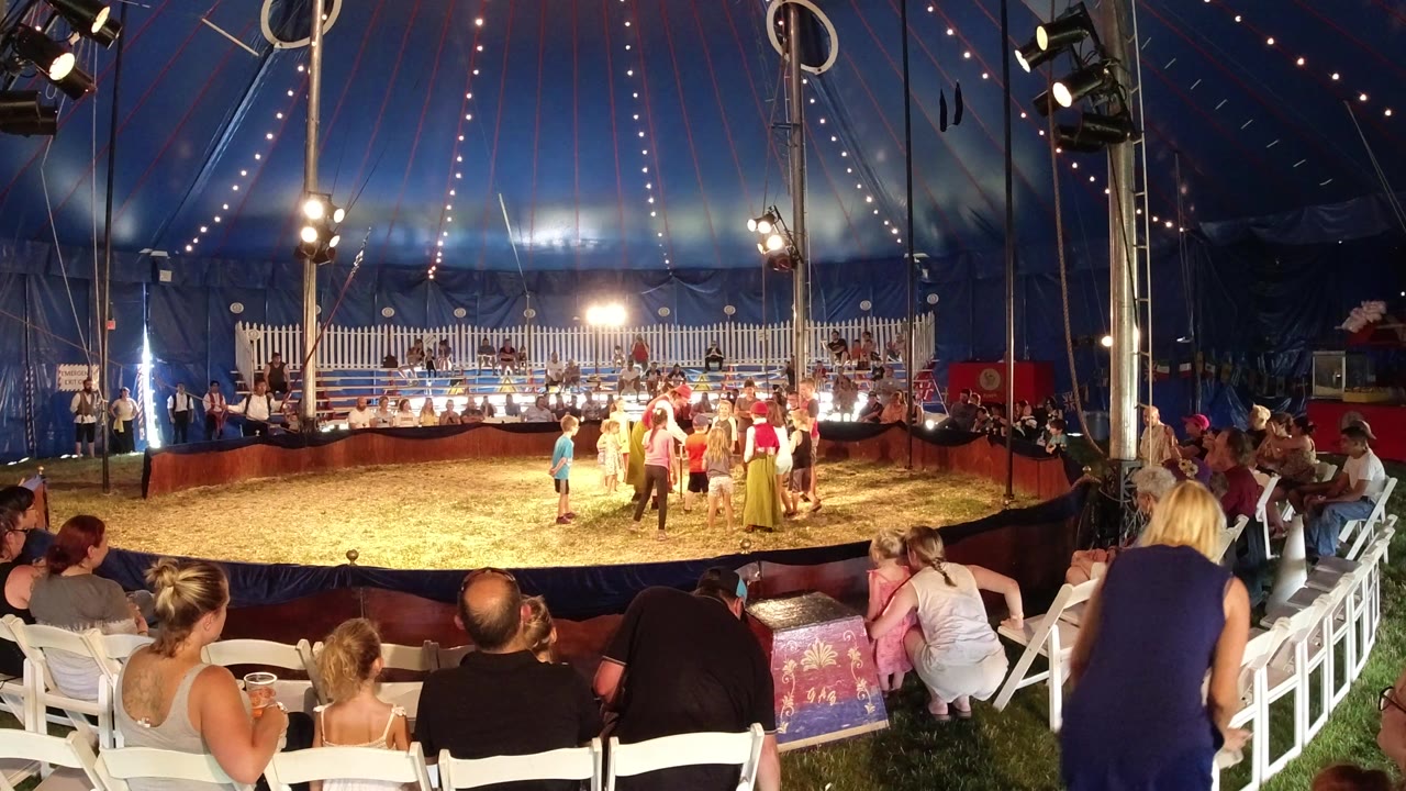Spectators watch children and adults in a tented sand ring.