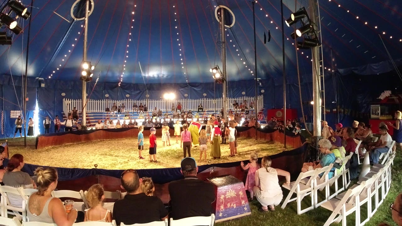 Audience watches children standing in a lit circus ring.