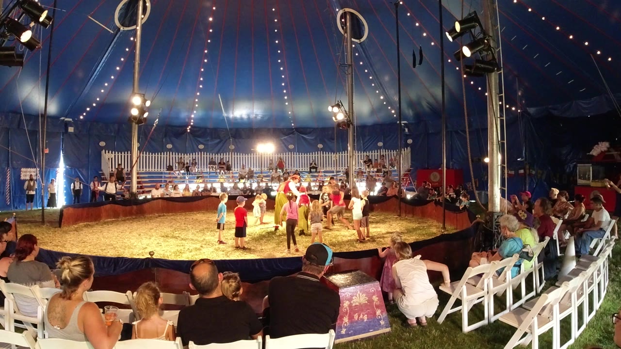 Wide circus tent view with audience and children near performers