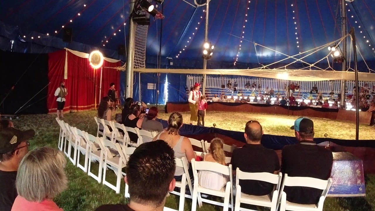In Broomfield, Colorado, spectators sit in white folding chairs as a clown stands near the center of a small circus tent ring under string lights.