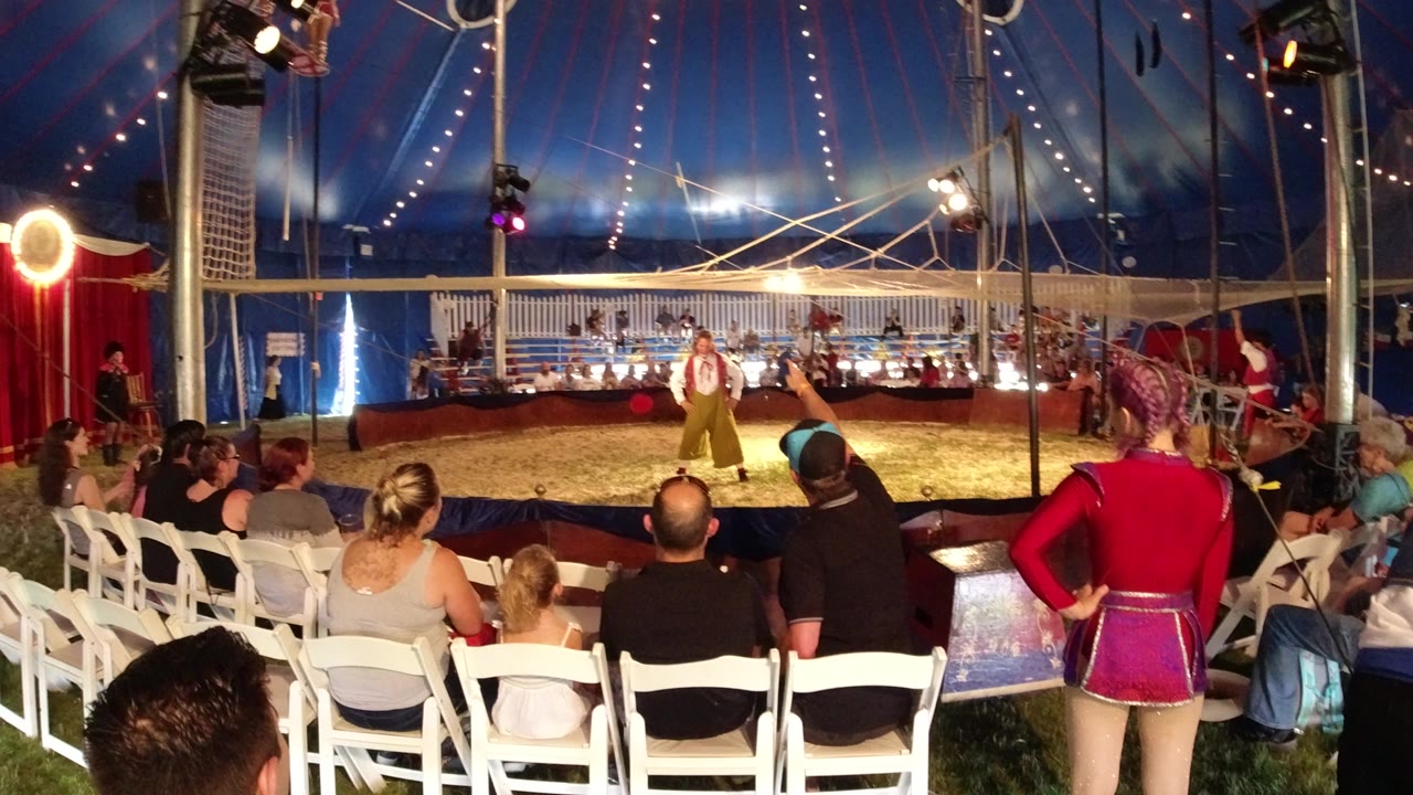 Audience seated around a tent performance ring with a costumed performer at center.