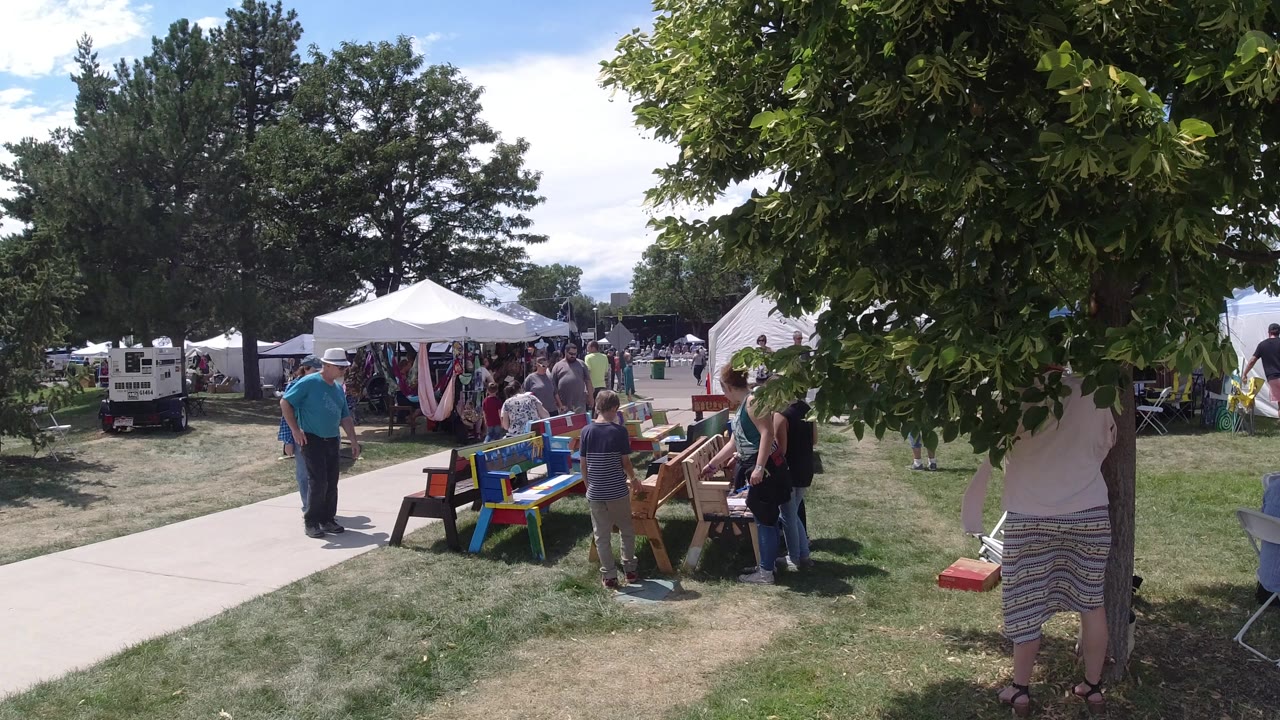 Outdoor gathering with people near colorful tables and white tents.