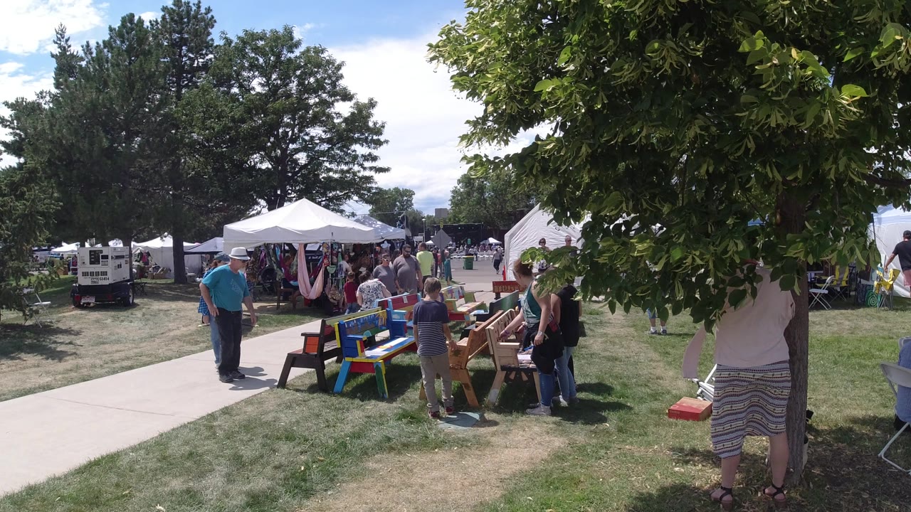 Broomfield, Colorado frame with a man in a blue shirt near a path, children and adults around painted tables, and white tents set across the grassy background.