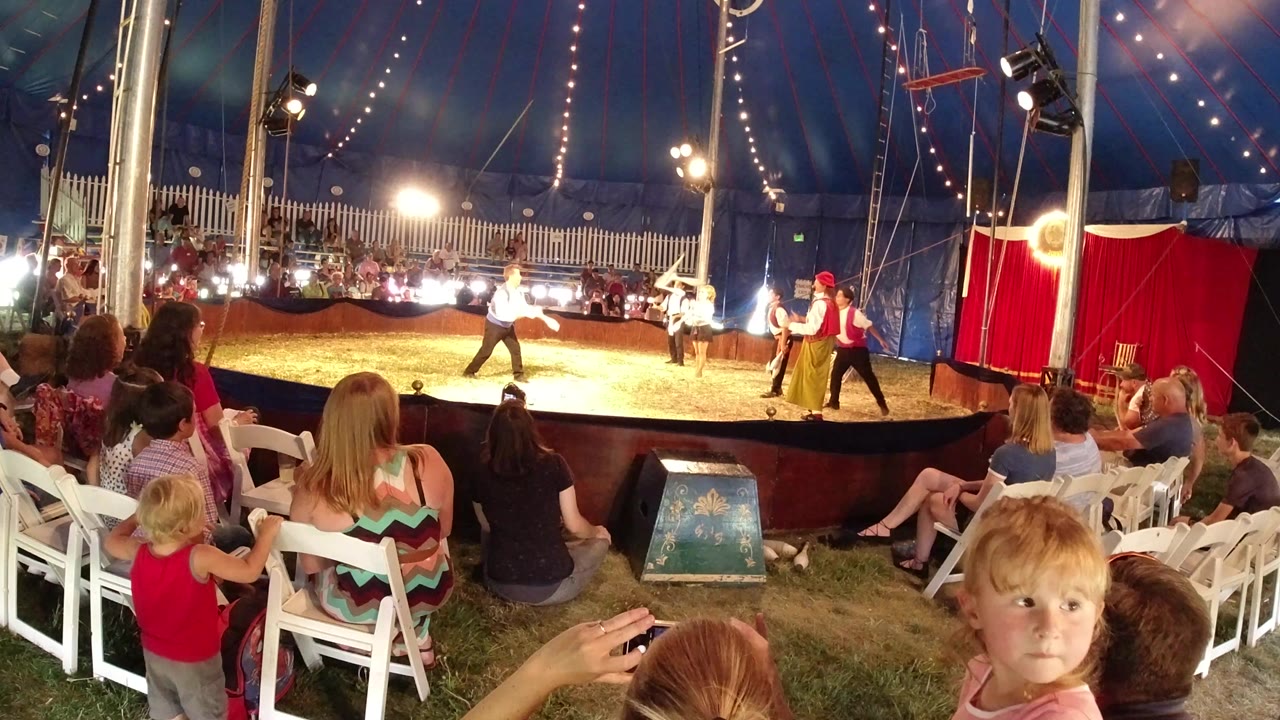 Circus performers juggling in a tent before a seated audience.
