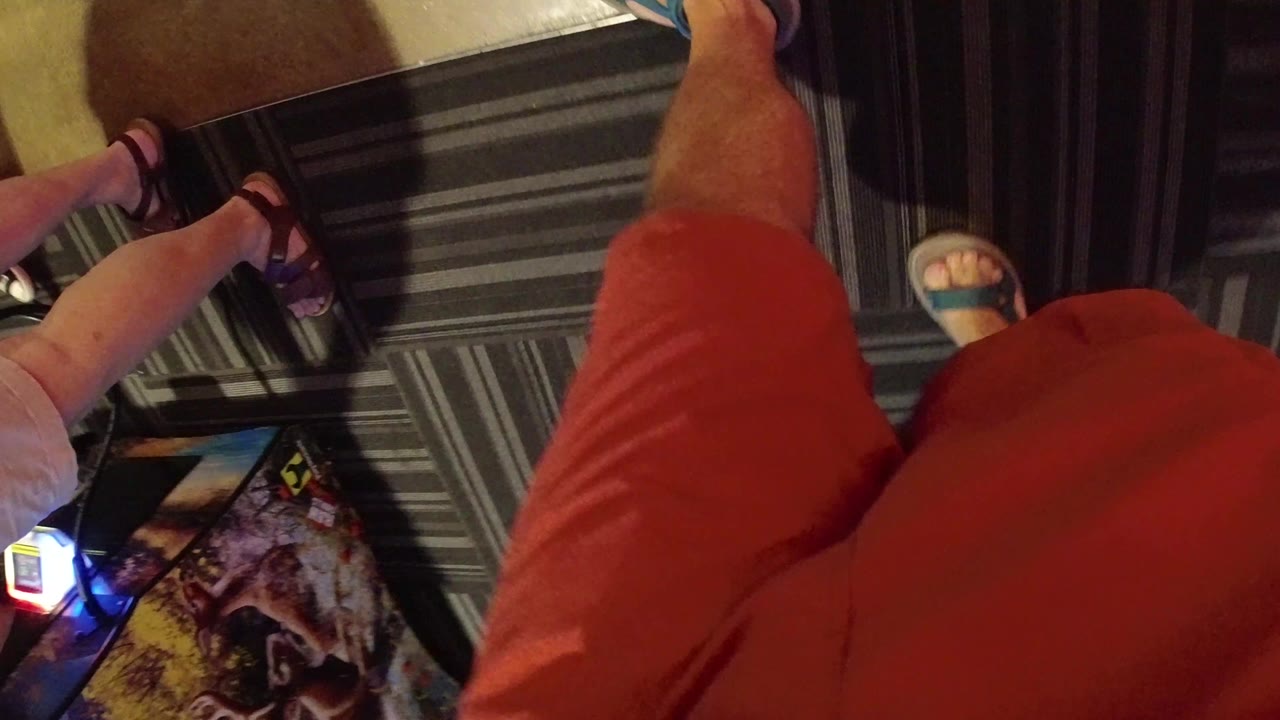 Downward view of legs, sandals, carpet tiles, and an arcade-like illuminated edge.