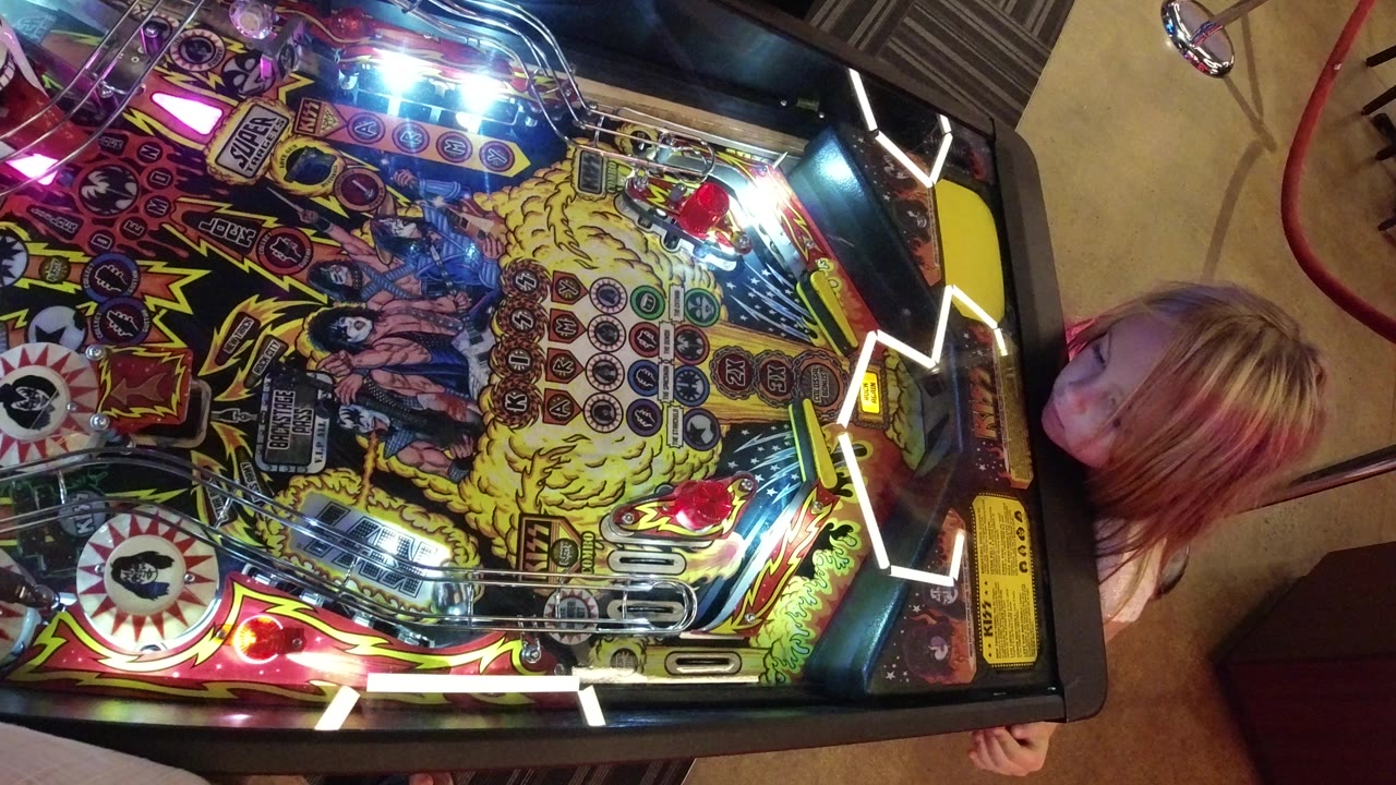 Child beside a colorful pinball machine viewed from above.