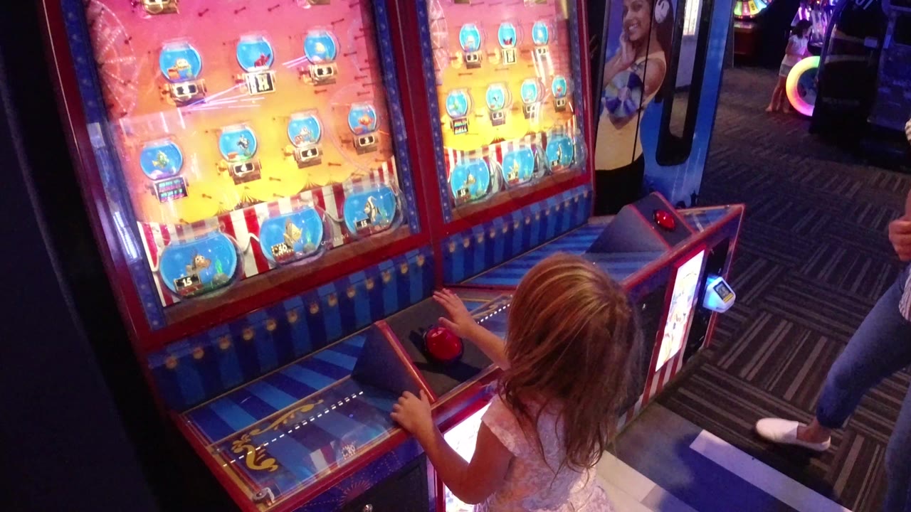 The child remains at the Broomfield arcade machine with one hand near the red button, while bright game panels and purple-blue indoor lighting frame the scene.