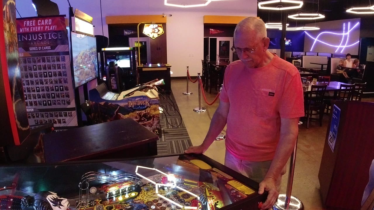 Older man playing a lit pinball machine in an arcade.
