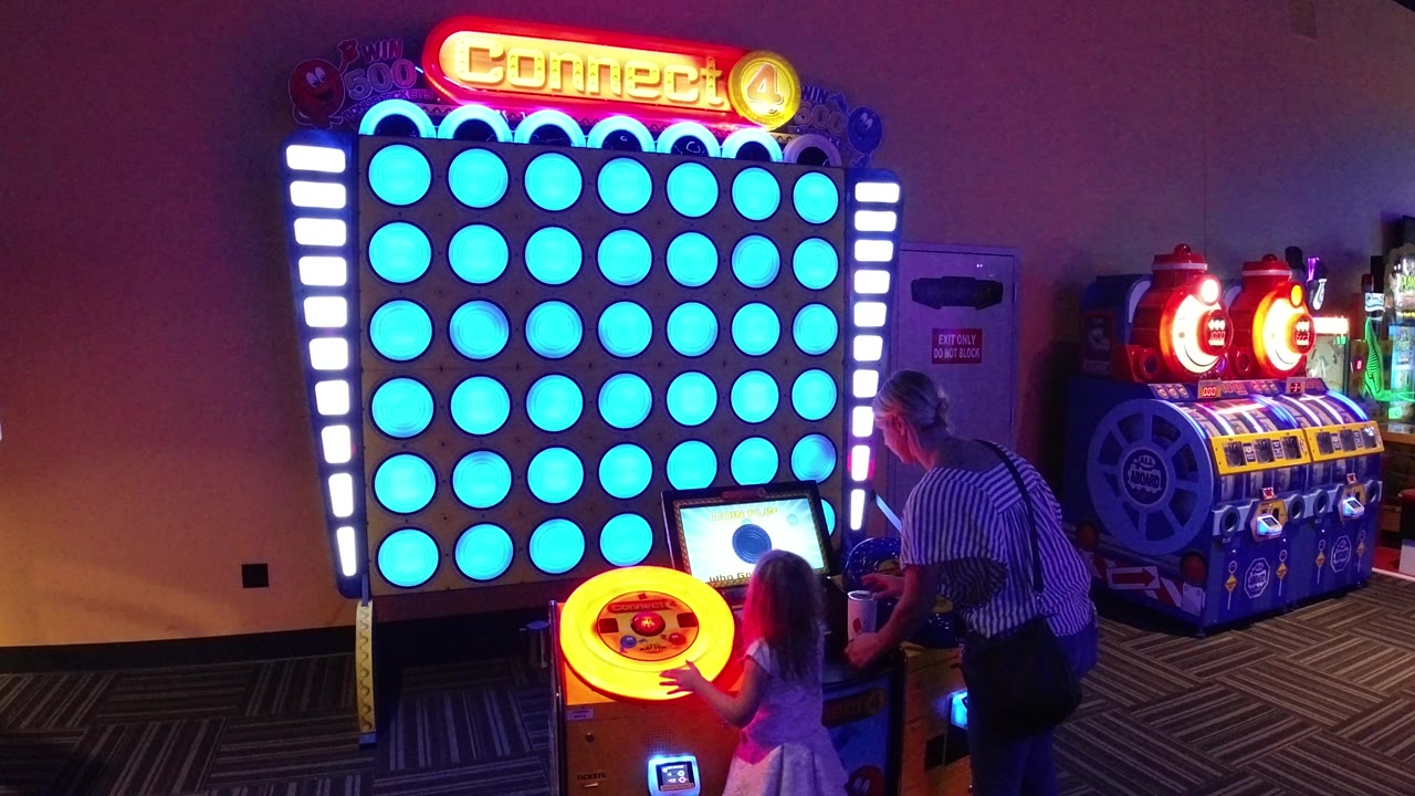 Child and adult at a glowing Connect 4 arcade game.