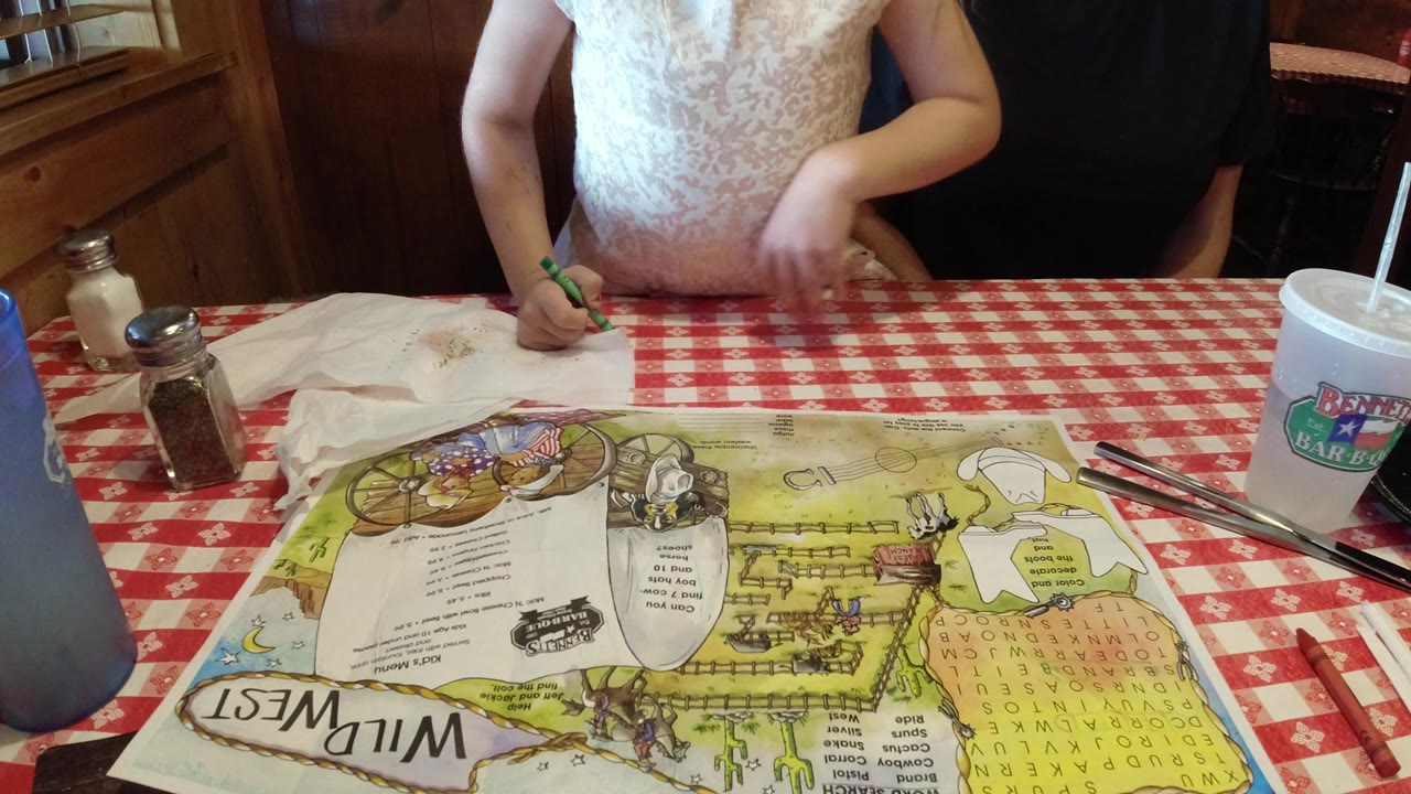 At the start of the Broomfield, Colorado clip, a young child holds a green crayon over a Wild West themed paper road map on a red checkered restaurant table, with the face mostly out of frame.