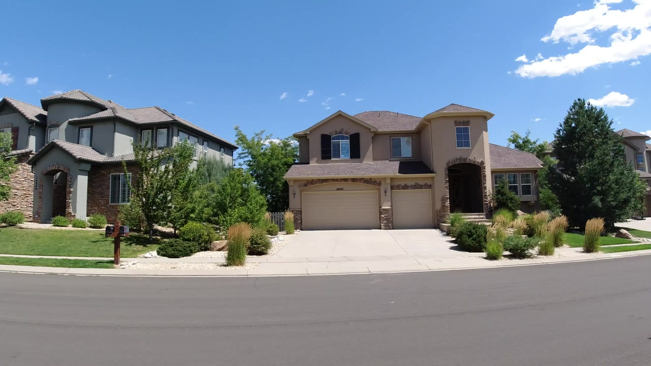 A Broomfield, Colorado residential street with two-story houses, garages, lawns, shrubs, and no visible people at the start of the clip.