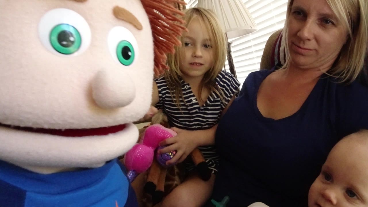 In Broomfield, Colorado, the puppet remains close to the lens as the child looks forward and the adult woman sits beside her in soft window light.