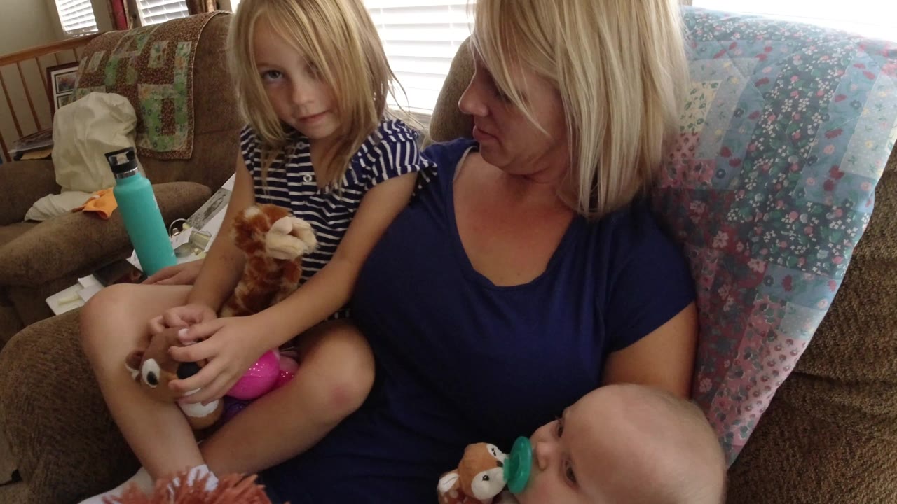 Mother seated with a young girl and baby in a rocking chair.