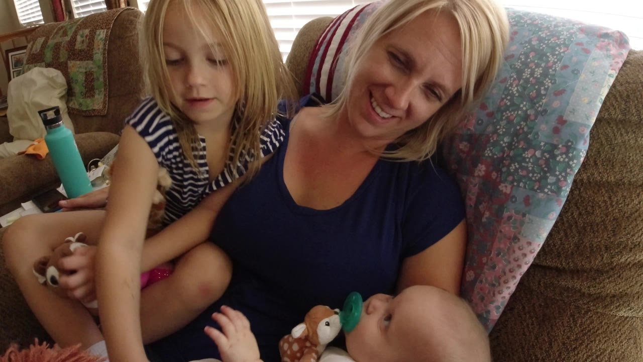 In Broomfield, Colorado, the child sits cross-legged with stuffed toys while the blonde woman smiles down toward the baby in her lap area.