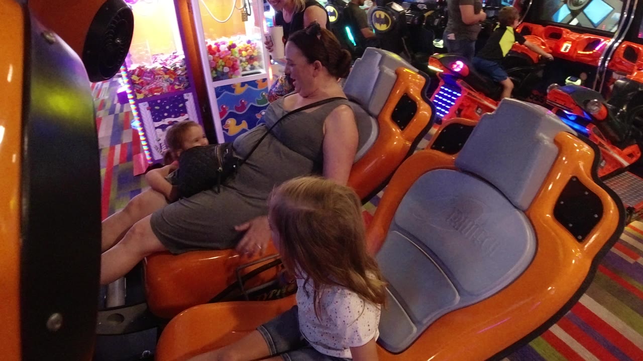 Woman and young girls beside an orange arcade ride seat.
