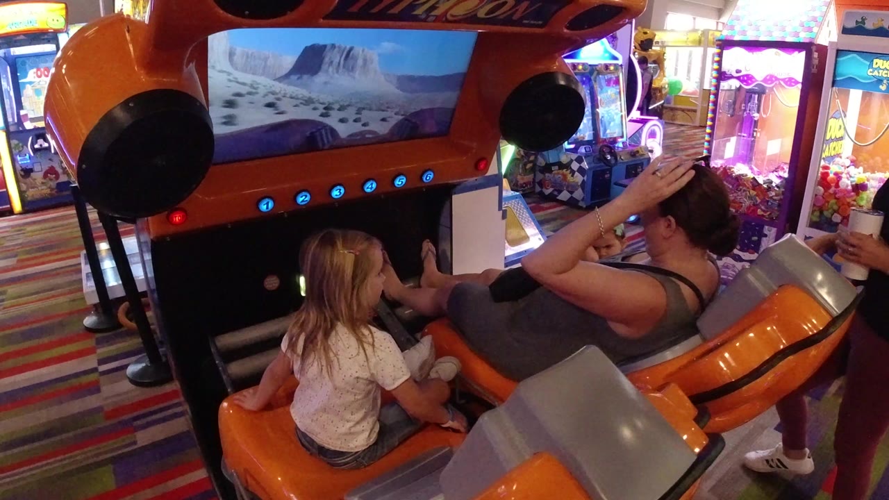 Child and adult seated at an orange arcade ride game.