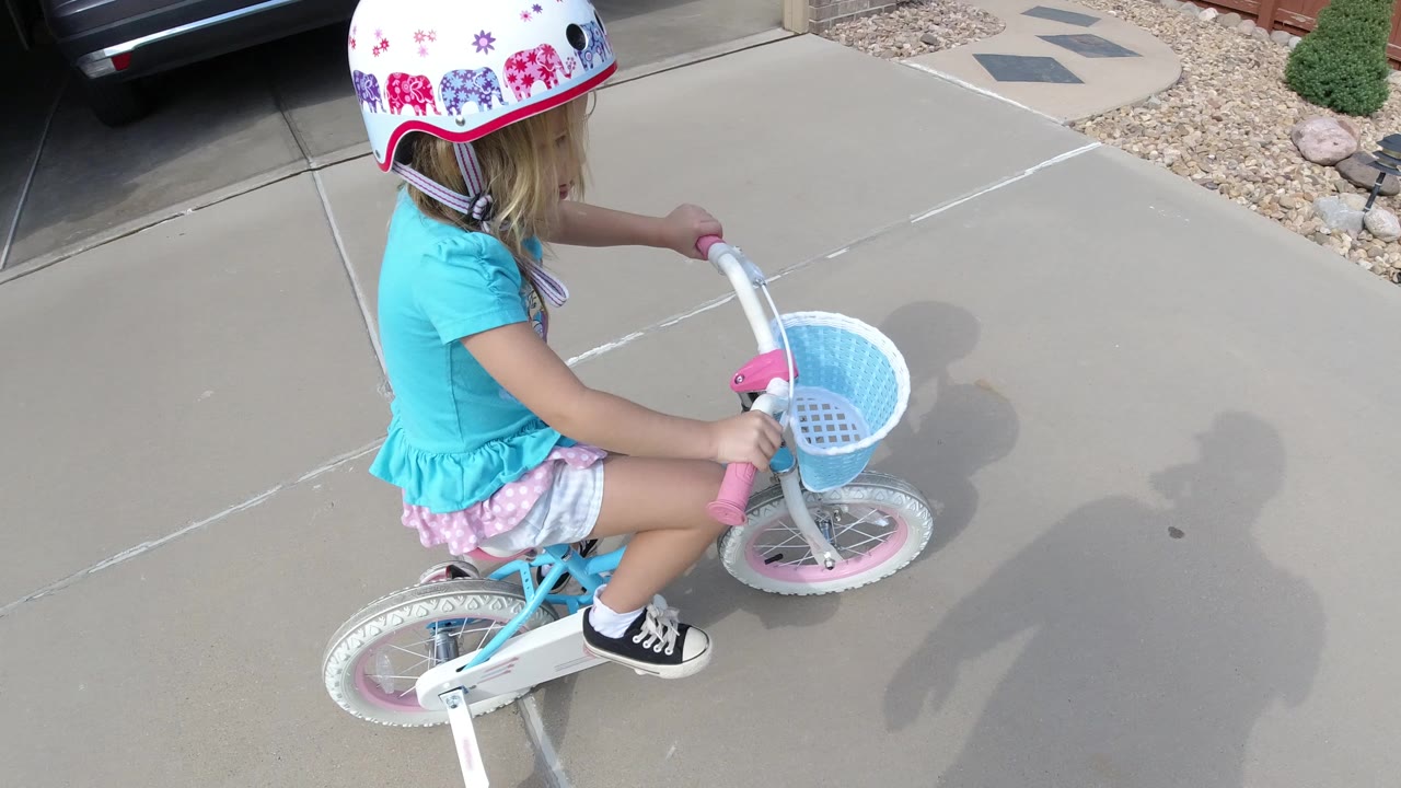 Child in a helmet rides a small bicycle on a concrete driveway.
