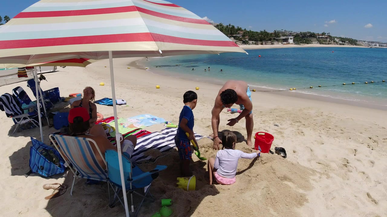 Family group under a striped umbrella on a sandy beach