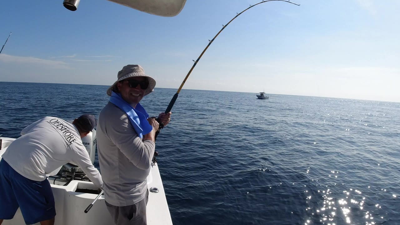 Man reeling a bent fishing rod on a boat with another person beside him