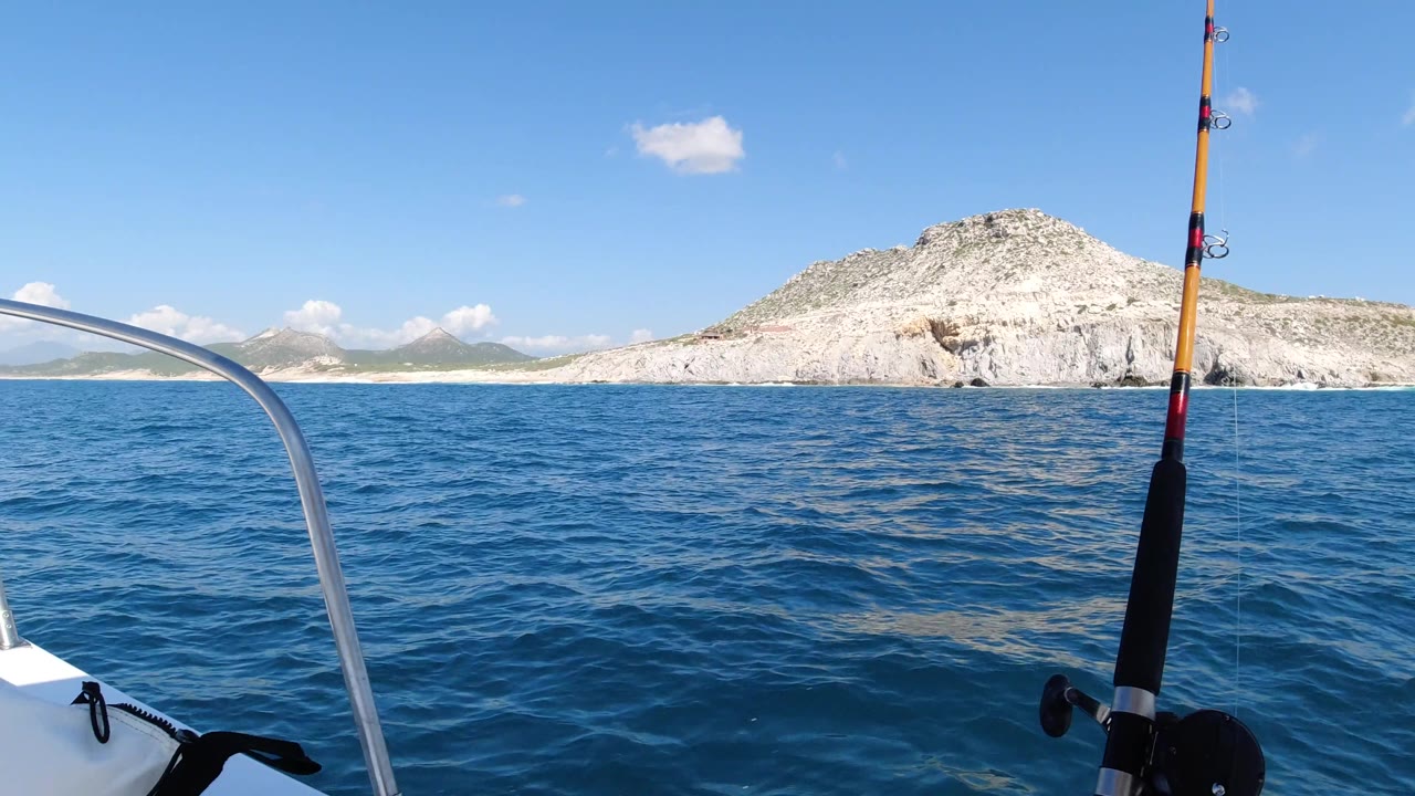 Fishing rod in foreground with open water and rocky coastal hill behind.