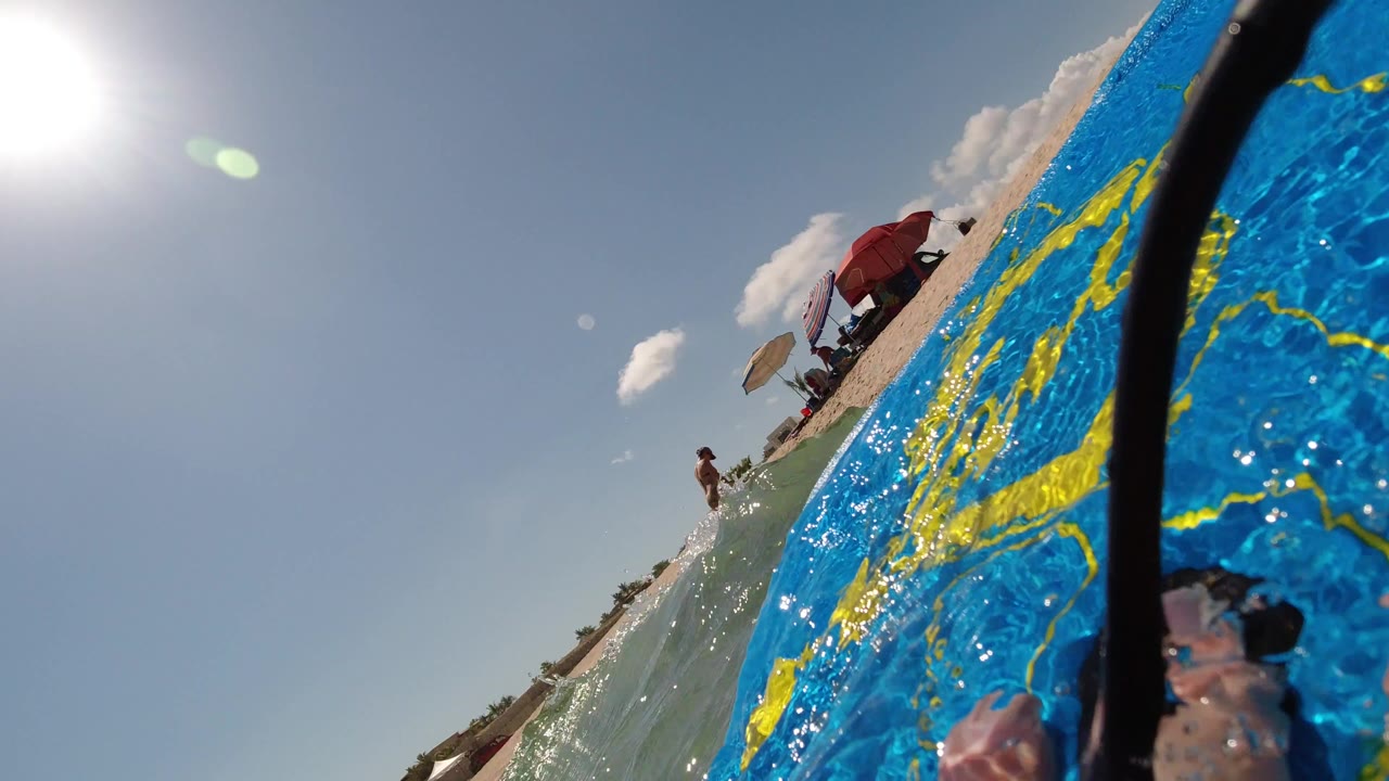 Blue board in ocean water with beach umbrellas and people in the background