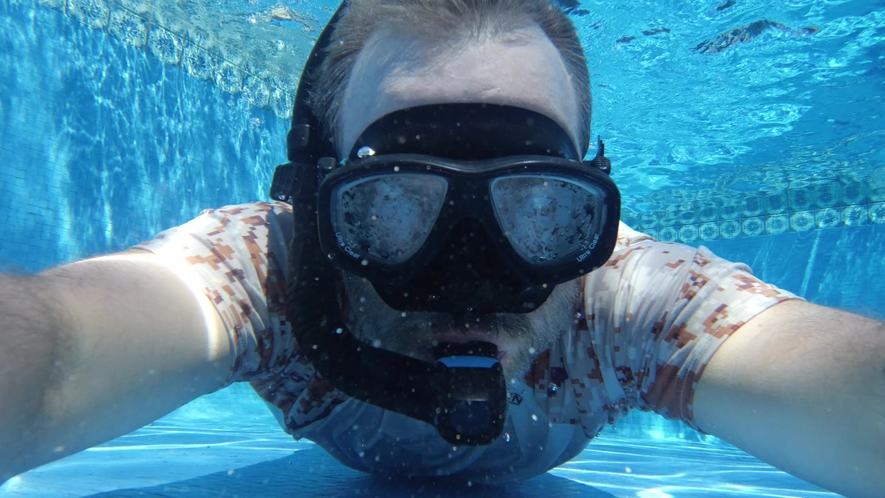 Underwater swimmer in a t-shirt wearing a black mask and mouthpiece.