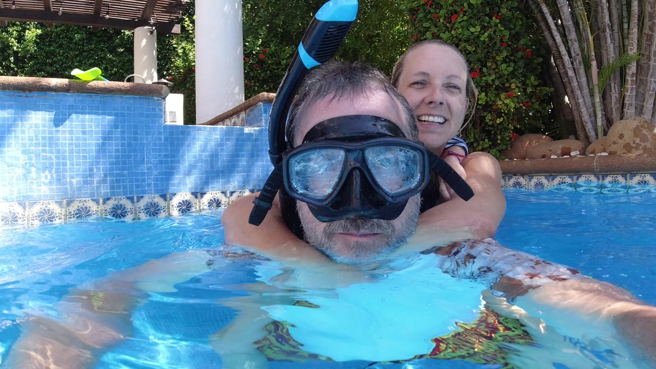 Man in snorkel mask with woman behind him in a resort pool.