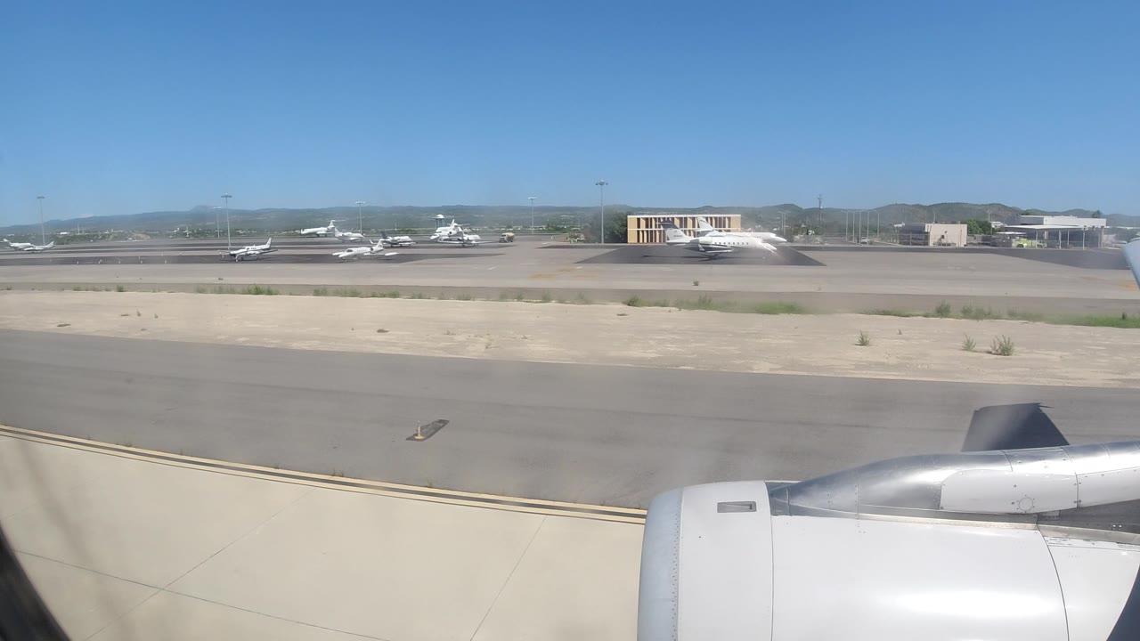Jet engine foreground with tarmac, terminal building, and planes in the distance.