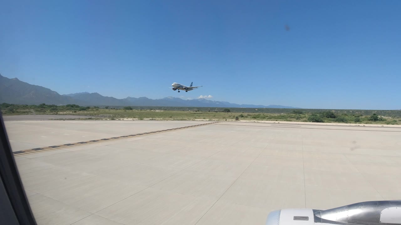 Aircraft over a wide runway with mountains beyond.