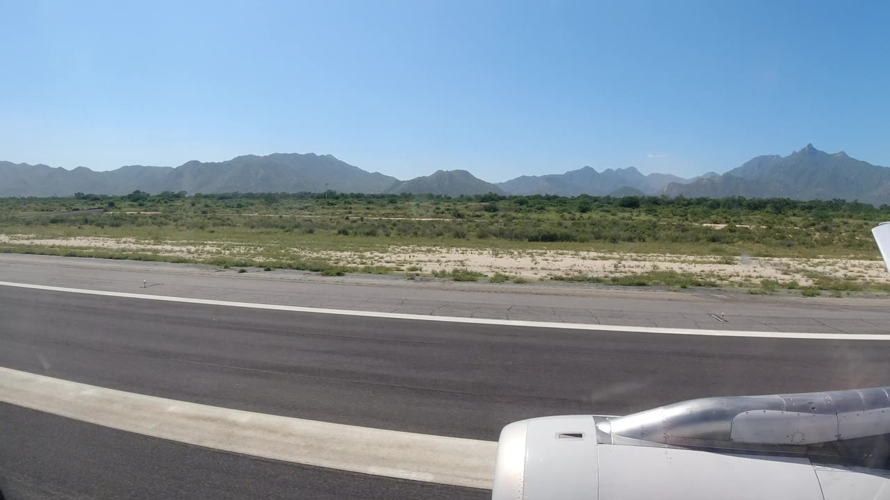 Runway and airplane engine with mountains under a clear sky.