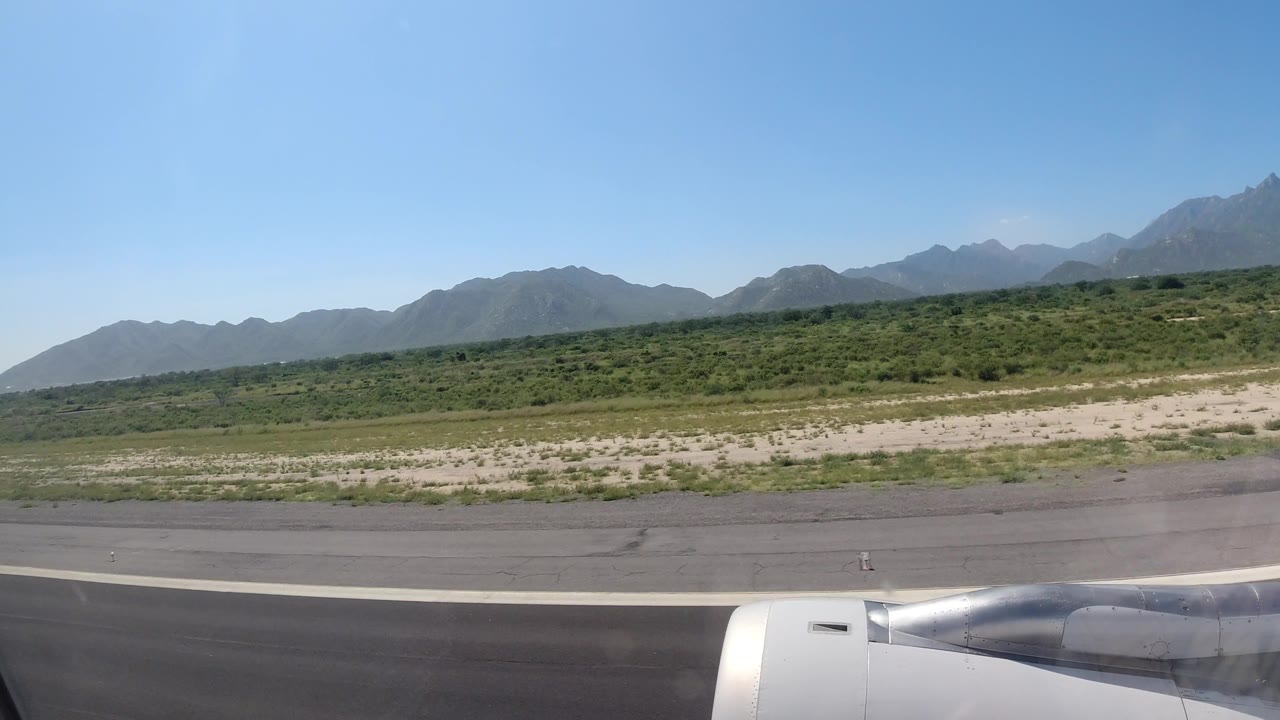 Aircraft engine over runway edge and low vegetation under mountain skyline.