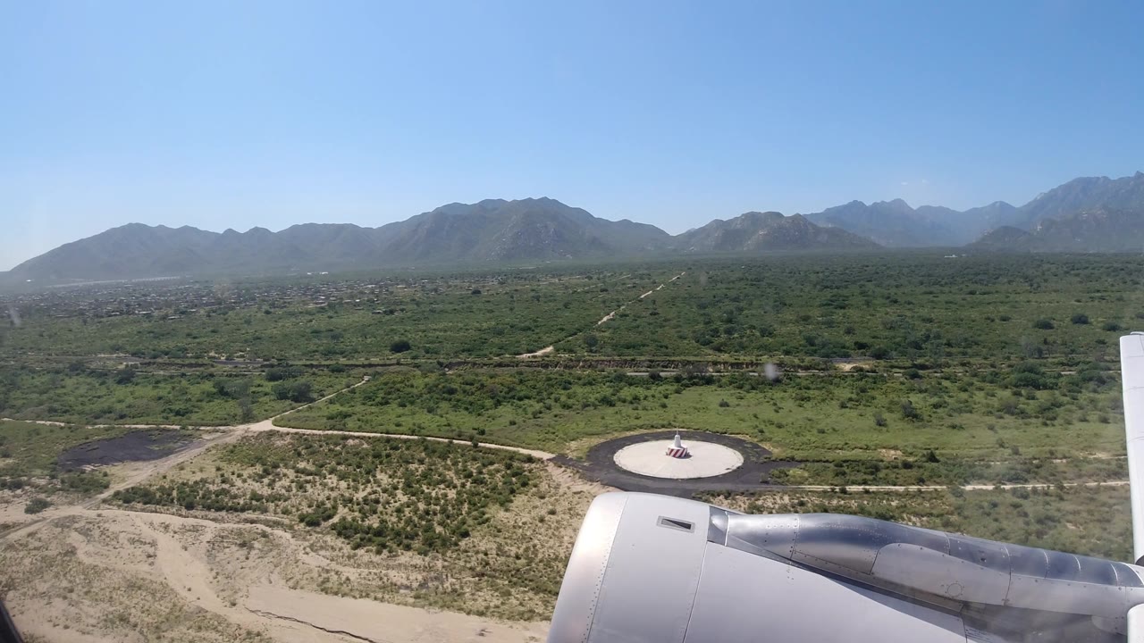 Airplane wing passing above a runway-side area and fields.