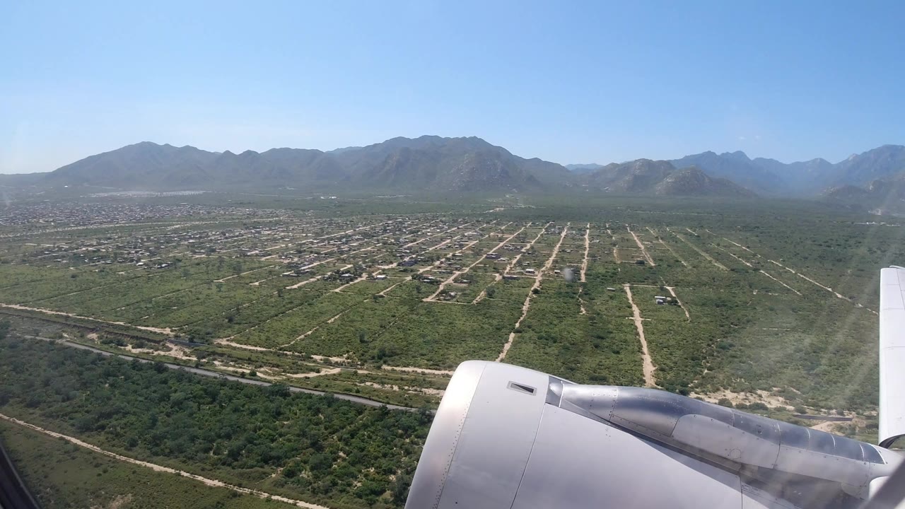Aircraft wing over green fields, roads, and mountains.