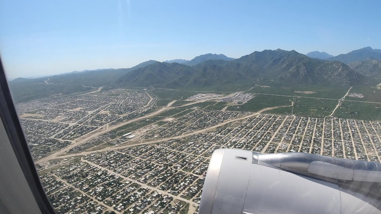 Airplane window view over a city grid and mountains with jet engine in foreground.
