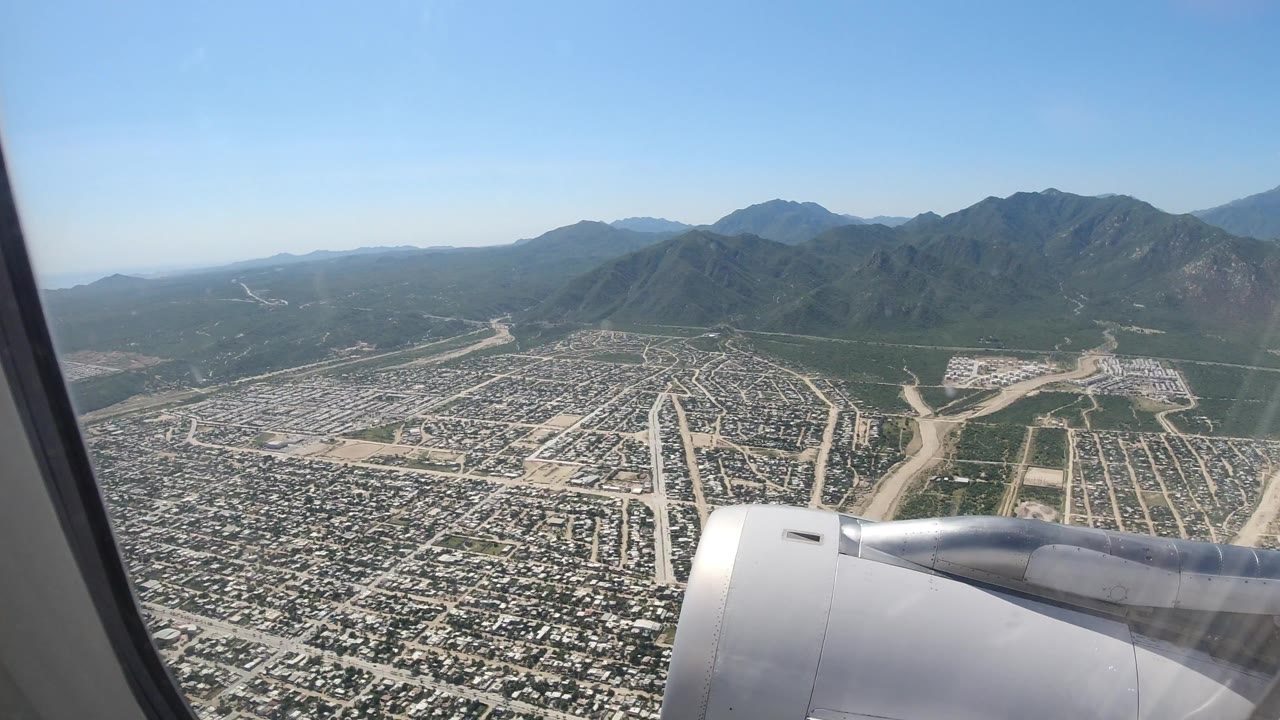 Airplane wing over a city grid with mountains beyond.