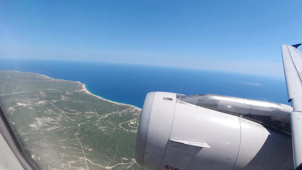 Airplane engine and wing over coastal land and blue ocean.