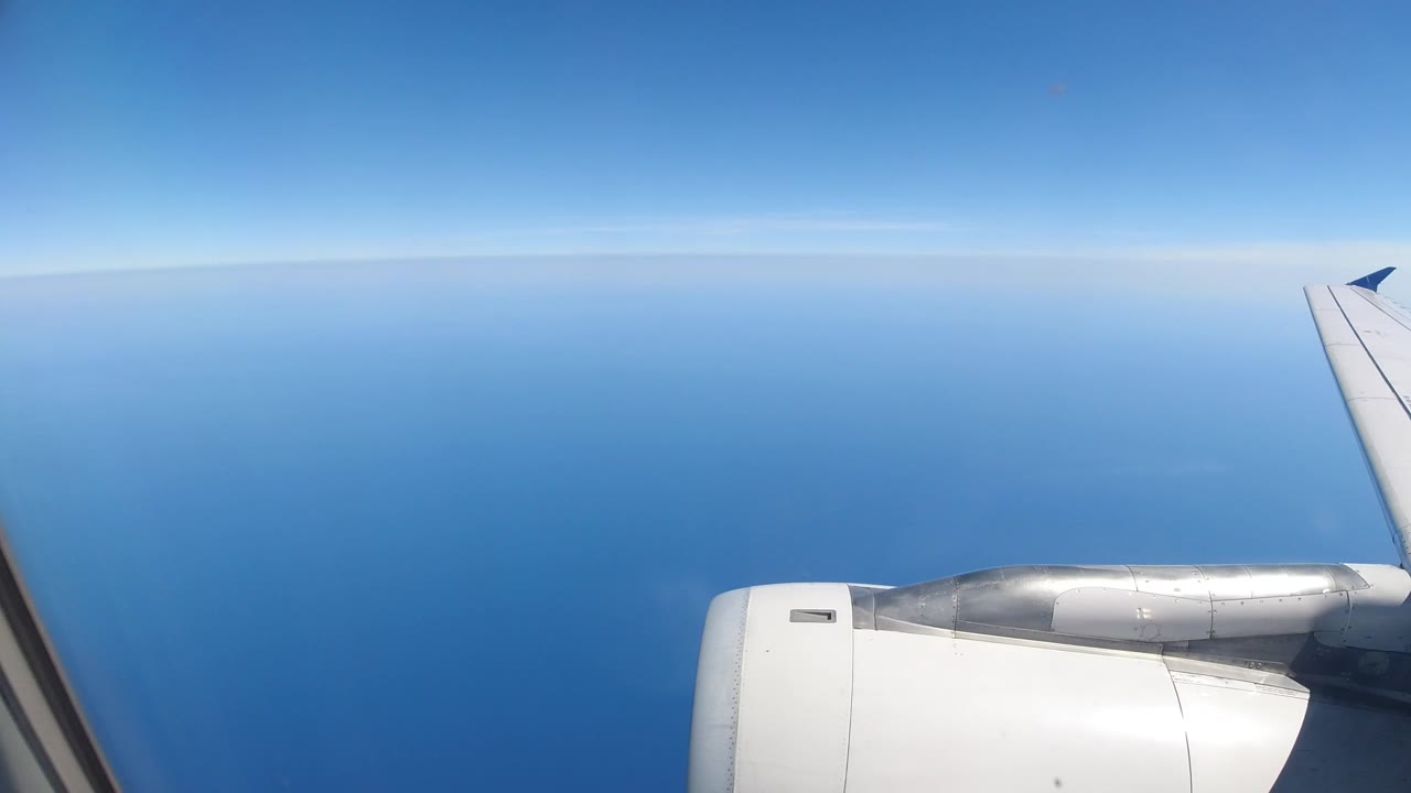 Jet engine and wing above blue ocean and sky