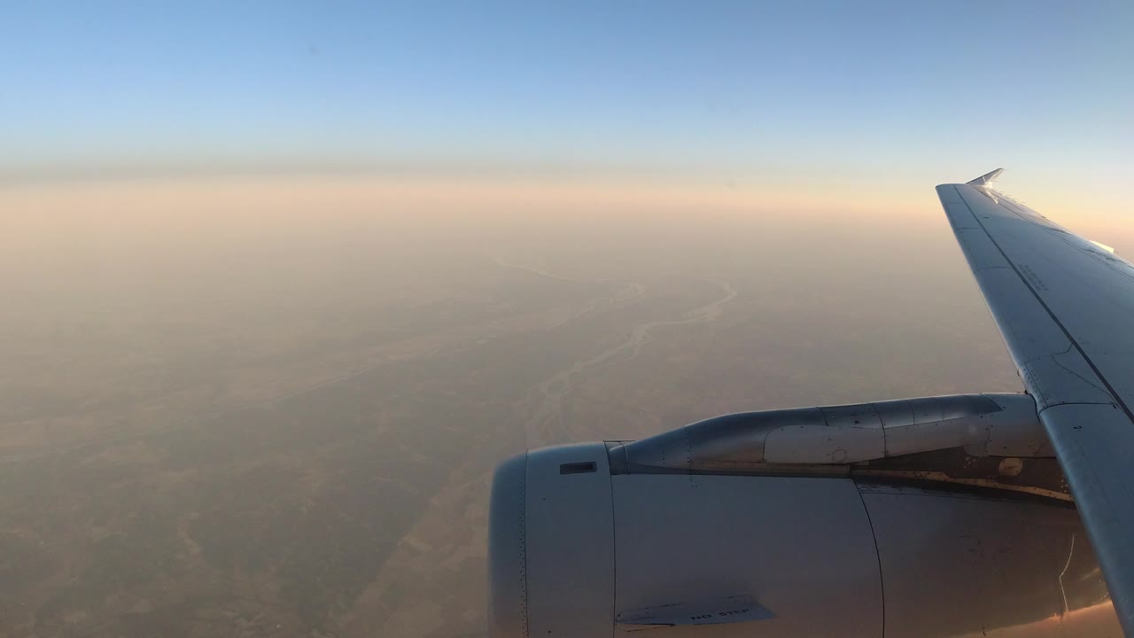 Passenger-window view of a plane wing over a muted landscape.