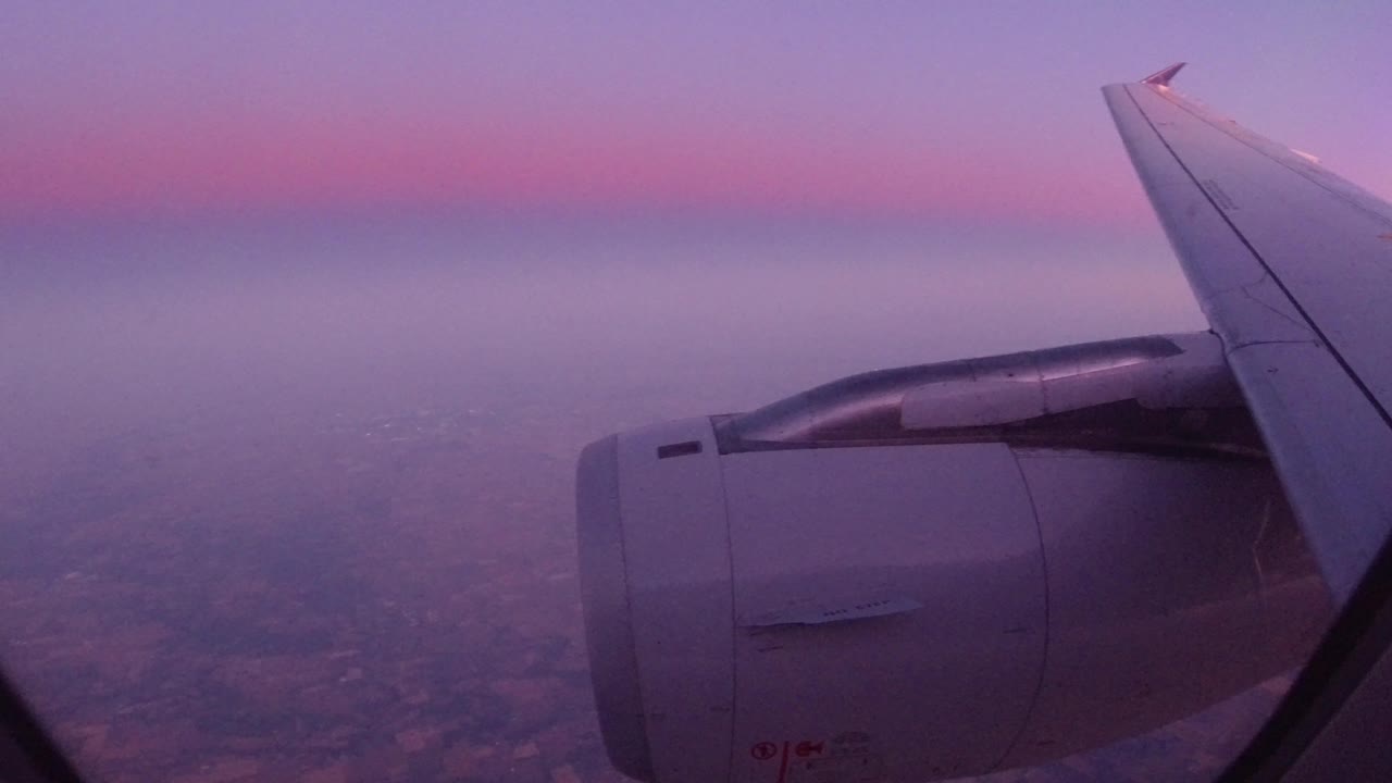 Airplane engine and wing over hazy land under pink sky.
