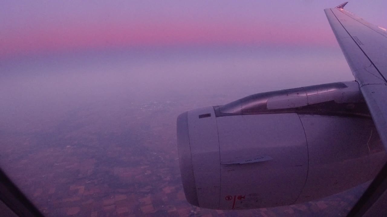 Airplane engine and wing over hazy terrain with a purple cloud layer.