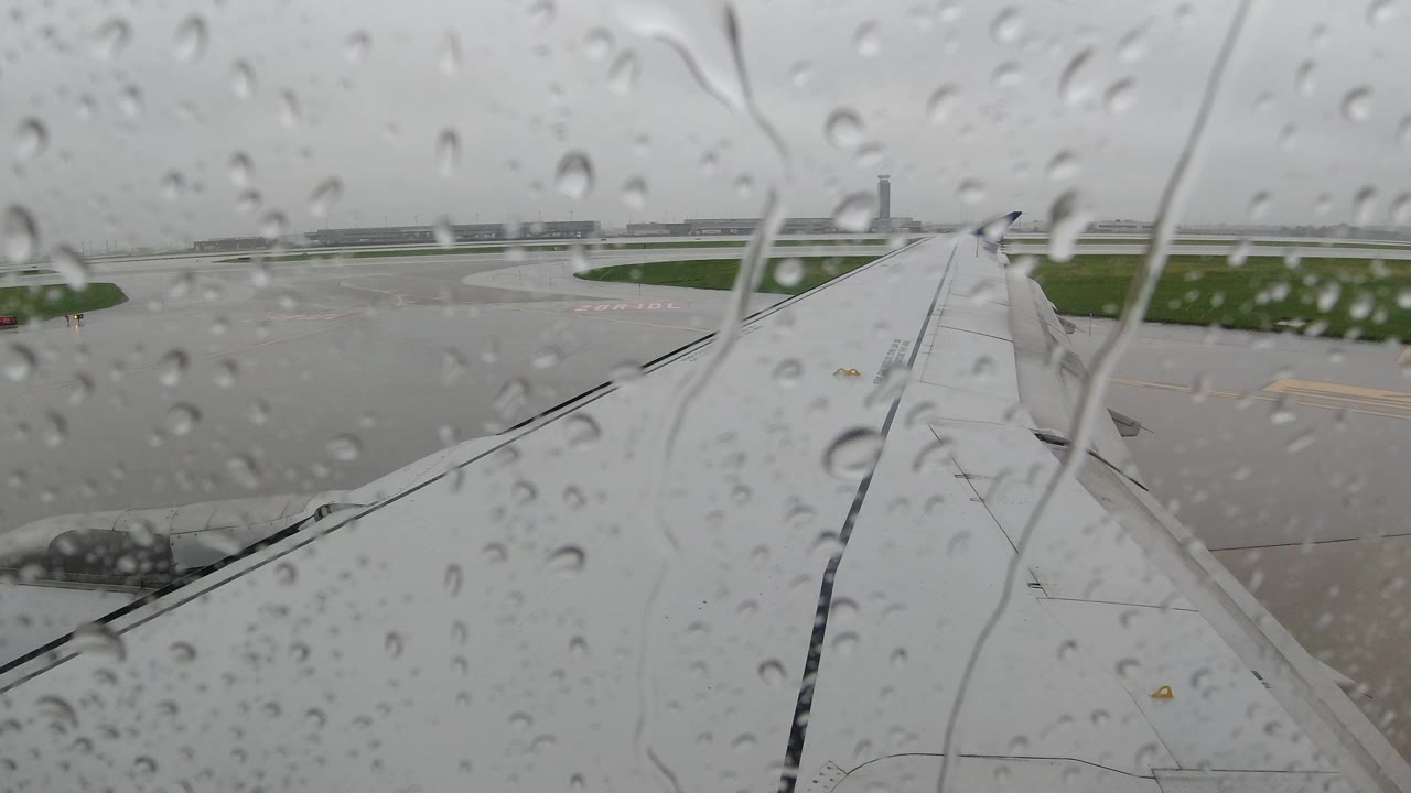 Rain-streaked glass in front of an airplane wing and wet airport ground.
