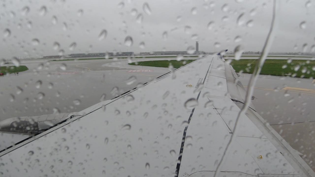 Raindrops cover the airplane window at the start of the Los Cabos, Mexico clip, with the white wing angled across gray tarmac and no visible people.