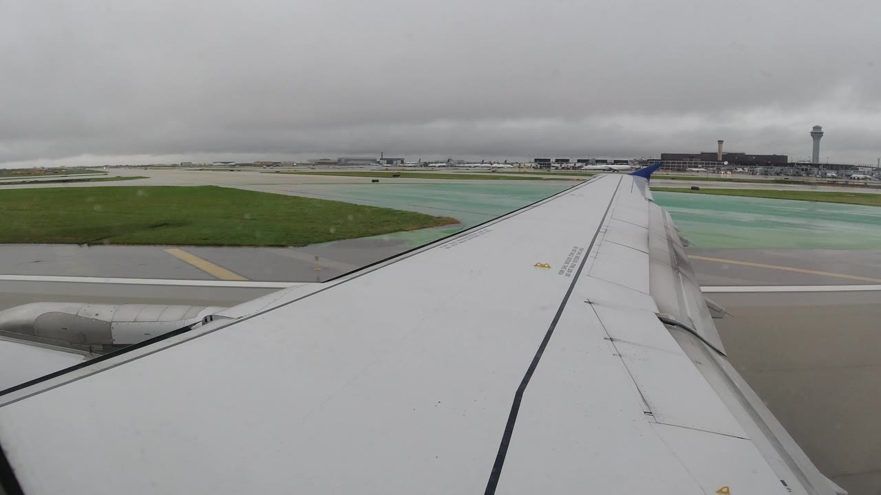 Airplane wing pointed toward airport buildings and tower.