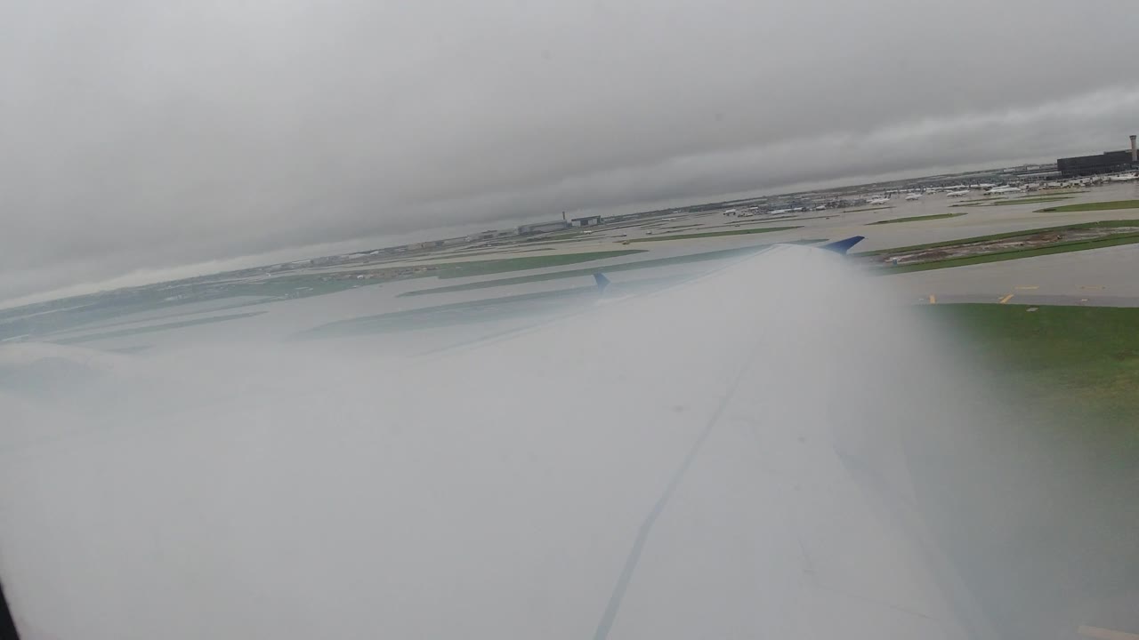 Airplane wing over wet airport runways under gray clouds.