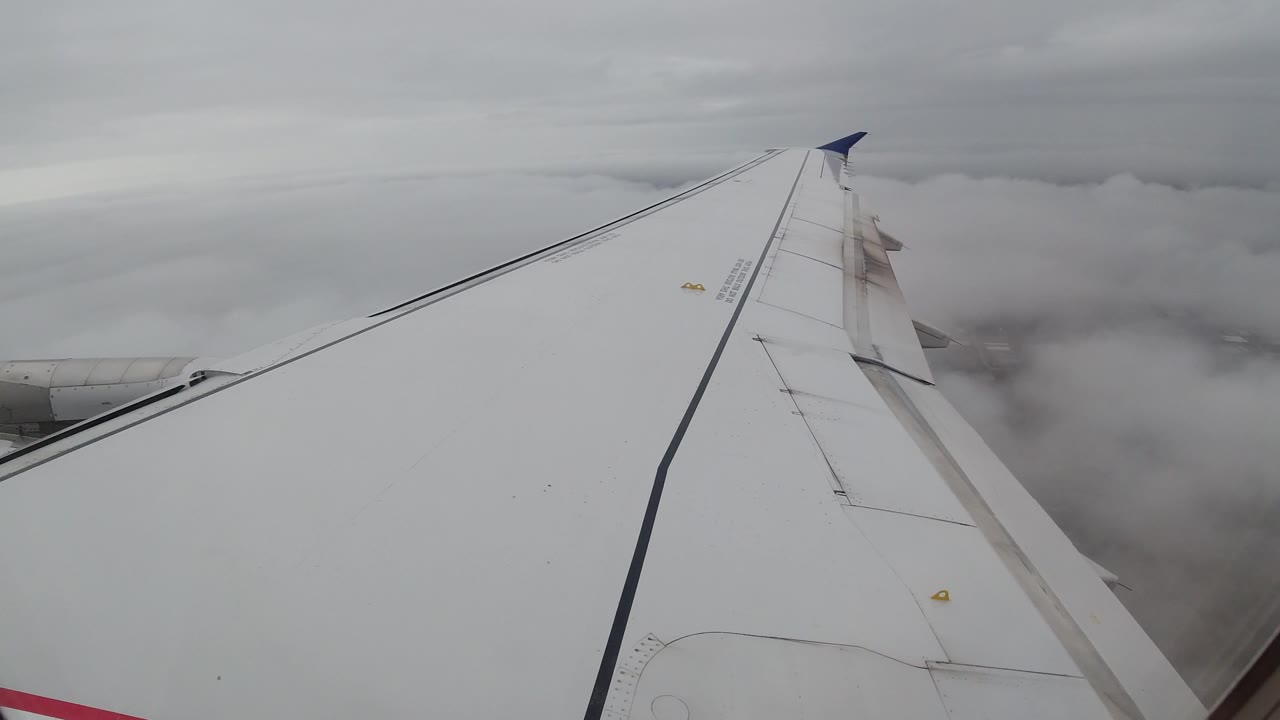 White airplane wing seen from a passenger-window angle above gray cloud cover near Los Cabos, Mexico, with no visible people.