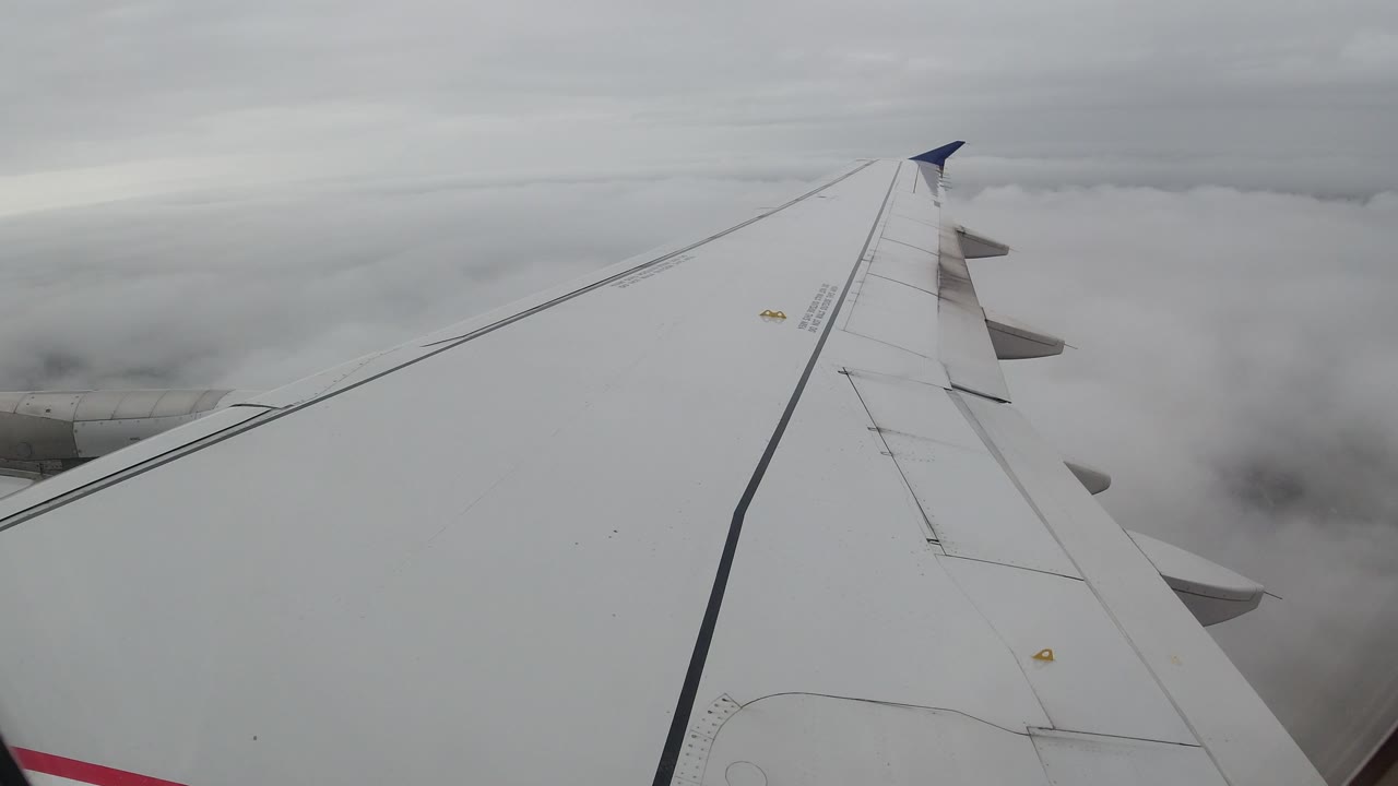 Plane wing seen above soft overcast clouds.